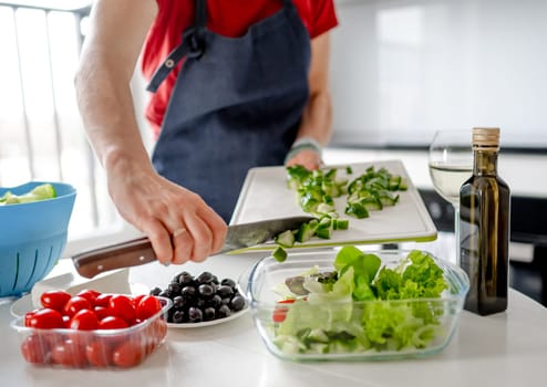 Girl Pours Chopped Cucumbers Into Bowl For Greek Salad At Home In Bright Kitchen