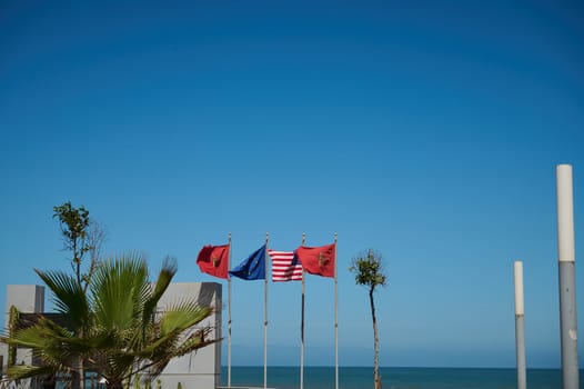 Background with flags of different countries on the promenade. Moroccan, Spanish, European Union, USA and Great Britain flags over blue sky and Atlantic ocean background
