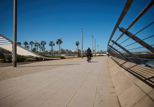 Rear view of unrecognizable person riding bicycle along the promenade marine. Cityscape