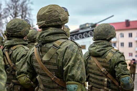 Several soldiers wearing camouflage uniforms stand in a row, holding guns and looking prepared for a mission. The background is blurred, highlighting their readiness and determination.