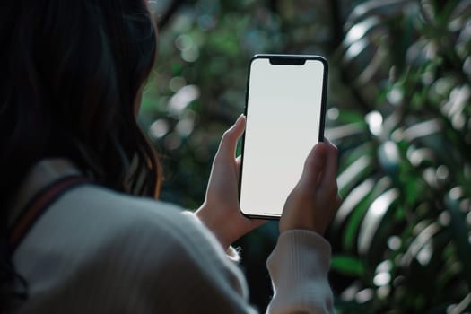 A woman is holding a portable communications device with a white screen in her hands, making a gesture with her finger and thumb. She is standing next to a tree, with eyelashes fluttering