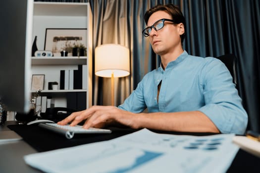 Smart businessman analyzing business paragraph dynamic database marketing analysis plan surrounded paper sheet and pc monitor report to compare with document data at home office at night. Pecuniary.