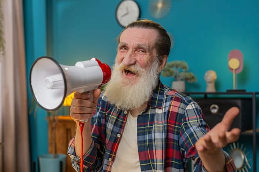 Senior bearded business man talking with megaphone announcing news loudly announcing advertising in home office. Mature grandfather manager warns using loudspeaker and shouting speech looks at camera