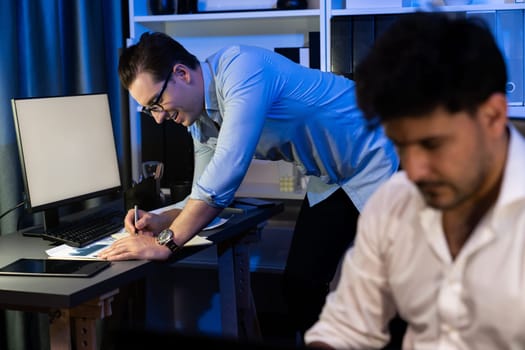 Colleagues concentrating on their job task at night home office behind desk while another man with thoughtful face solving to postpone the deadline of project at the blurred front side. Sellable.