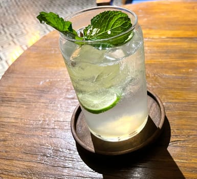 Selective focus, Delicious refreshing summer mojito with ice, lime and mint in a glass with grops. wood background. Copy space. Cold lemonade, tonic.