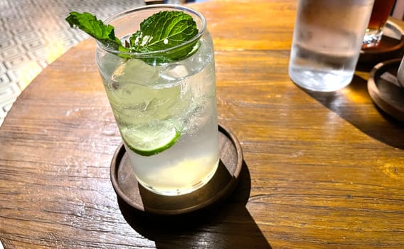 Selective focus, Delicious refreshing summer mojito with ice, lime and mint in a glass with grops. wood background. Copy space. Cold lemonade, tonic.