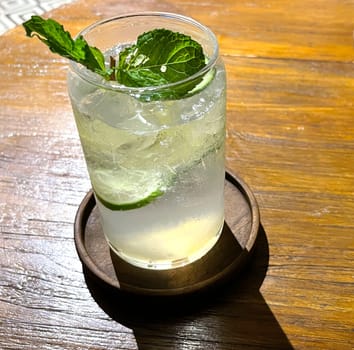 Selective focus, Delicious refreshing summer mojito with ice, lime and mint in a glass with grops. wood background. Copy space. Cold lemonade, tonic.