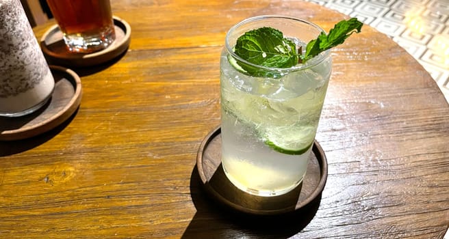Selective focus, Delicious refreshing summer mojito with ice, lime and mint in a glass with grops. wood background. Copy space. Cold lemonade, tonic.