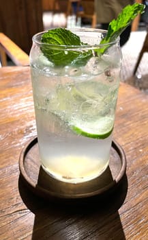 Selective focus, Delicious refreshing summer mojito with ice, lime and mint in a glass with grops. wood background. Copy space. Cold lemonade, tonic.