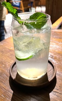 Selective focus, Delicious refreshing summer mojito with ice, lime and mint in a glass with grops. wood background. Copy space. Cold lemonade, tonic.