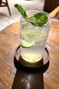 Selective focus, Delicious refreshing summer mojito with ice, lime and mint in a glass with grops. wood background. Copy space. Cold lemonade, tonic.