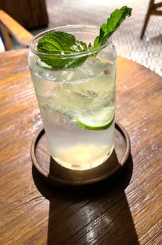 Selective focus, Delicious refreshing summer mojito with ice, lime and mint in a glass with grops. wood background. Copy space. Cold lemonade, tonic.