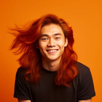 Handsome young male guy smile Asian with long red hair, on yellow orange background, banner, copy space, portrait. Advertising of cosmetic products, spa treatments, shampoos and hair care products, dentistry and medicine, perfumes and cosmetology men