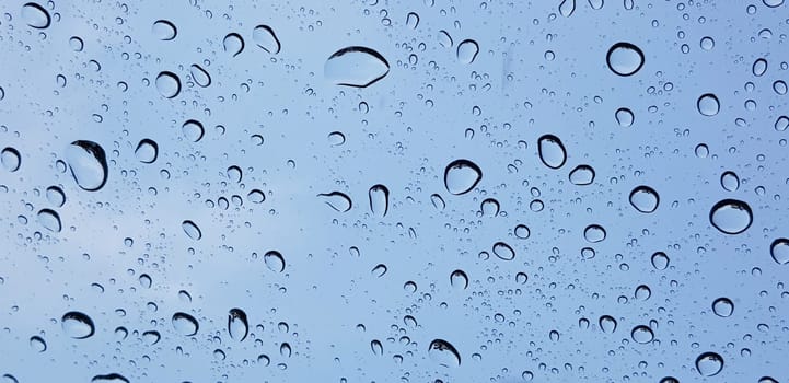 Water droplets perspective through window glass surface against blue sky good for multimedia content backgrounds