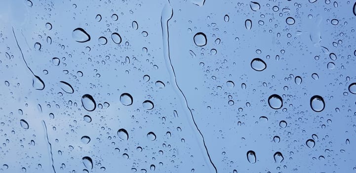 Water droplets perspective through window glass surface against blue sky good for multimedia content backgrounds