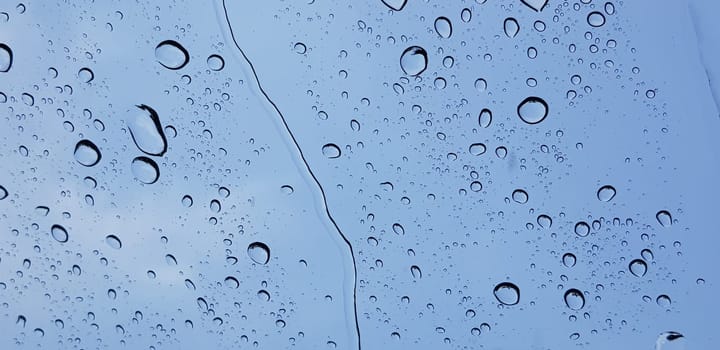 Water droplets perspective through window glass surface against blue sky good for multimedia content backgrounds