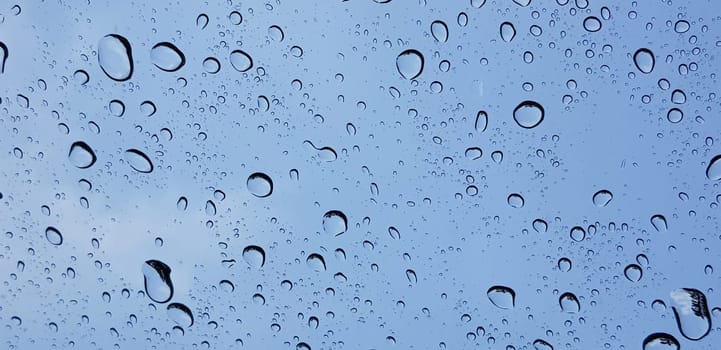 Water droplets perspective through window glass surface against blue sky good for multimedia content backgrounds