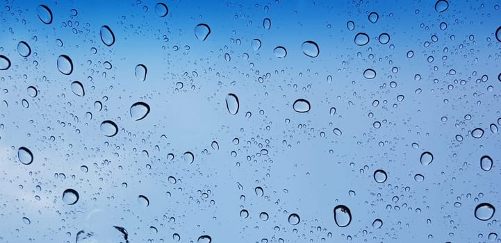 Water droplets perspective through window glass surface against blue sky good for multimedia content backgrounds