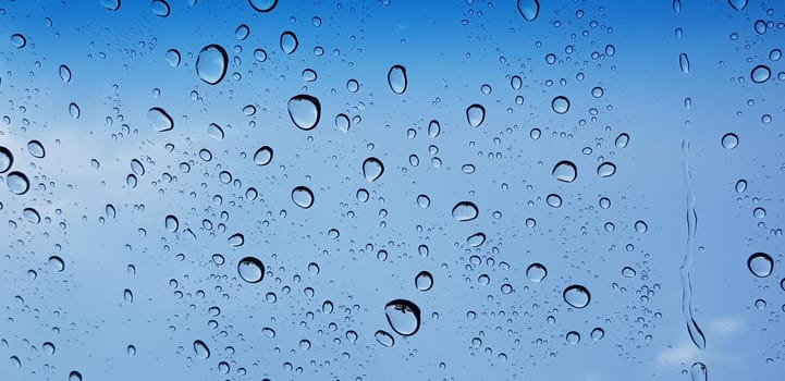 Water droplets perspective through window glass surface against blue sky good for multimedia content backgrounds