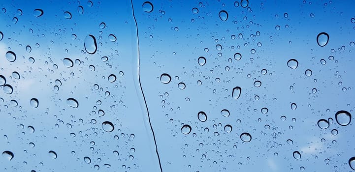 Water droplets perspective through window glass surface against blue sky good for multimedia content backgrounds