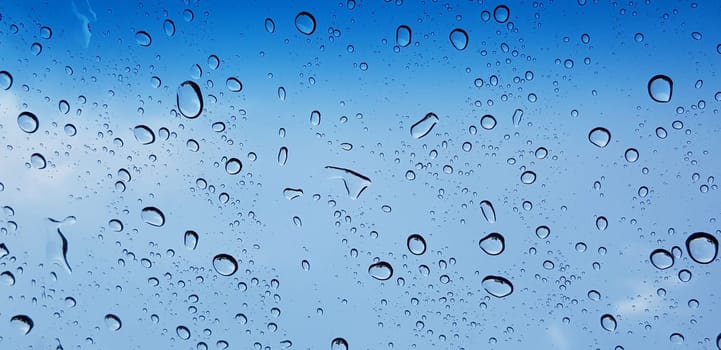 Water droplets perspective through window glass surface against blue sky good for multimedia content backgrounds