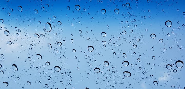 Water droplets perspective through window glass surface against blue sky good for multimedia content backgrounds