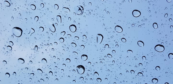 Water droplets perspective through window glass surface against blue sky good for multimedia content backgrounds