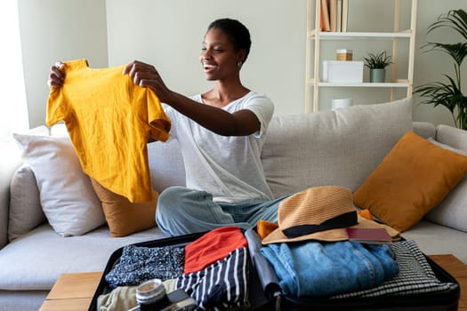 African American young woman folding t-shirt, packing suitcase for summer holiday trip. Holiday, tourist, vacation concept.