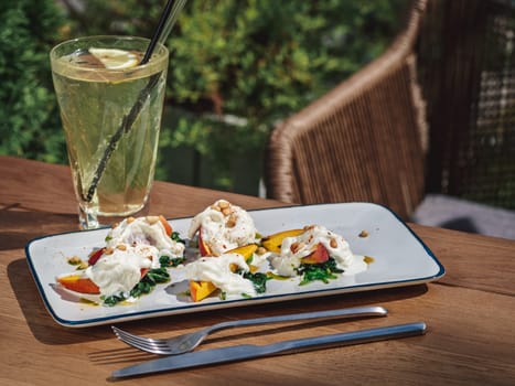 Delicious grilled nectarines and sauteed spinach with stracciatella cheese on plate. Tasty sweet dessert in summer sunny day outdoor of restaurant or cafe terrace