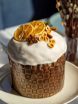 Delicious Easter cake with sugar glaze decorated orange slices, cinnamon and star anise, nuts, close up. Festive orthodox easter cake kulich on the table and willow on background