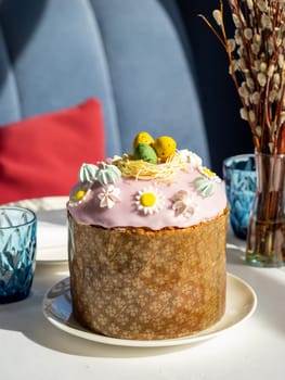 Delicious Easter cake with sugar glaze decorated chocolate eggs and merengue, close up. Festive orthodox easter cake kulich on the table and willow on background
