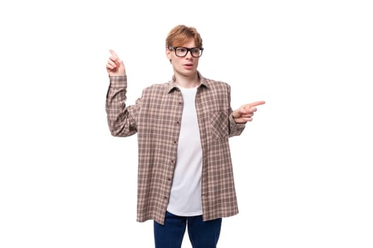 young European man with red hair in glasses and a plaid shirt shows his hands in different directions in surprise.