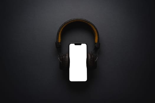 Retro style wireless over-ear headphones and smartphone with blank screen on dark gray background