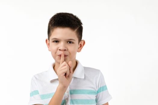 cute little boy in t-shirt asking to be quiet with finger on lips on white background. child showing shh sign