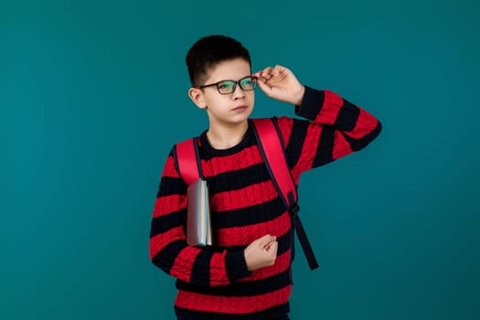 little cheerful school boy wearing glasses holding a book over blue background