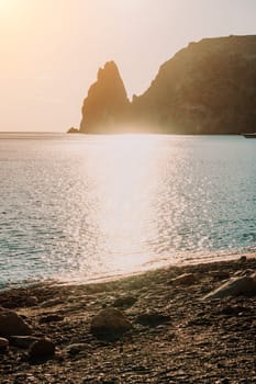 A red burning sunset with the silhouette of a cliff over the sea. Abstract nature summer or spring ocean sea background. Small waves on golden warm water surface with bokeh lights from sun.