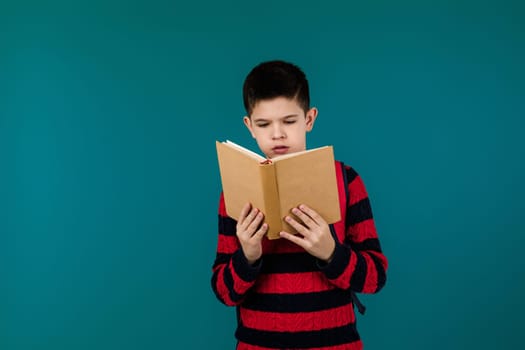 little cheerful school boy reading book over blue background, copy space. School concept.
