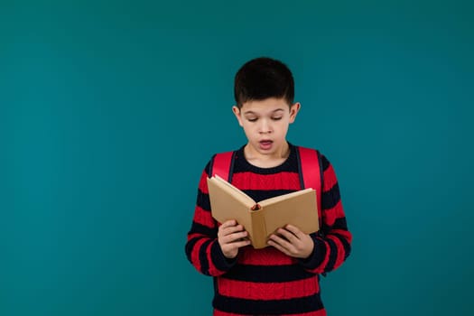 little cheerful school boy reading interesting book over blue background, copy space. School concept.