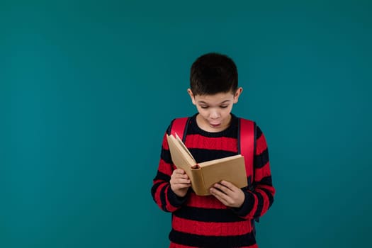 little cheerful school boy reading interesting book over blue background, copy space. School concept.