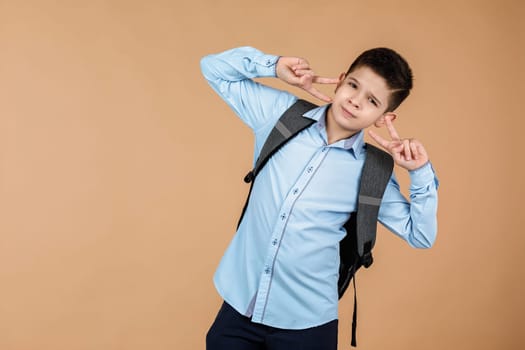Cheerful smiling little school boy with gray backpack having fun over soft yellow background. copy space. Back to school.