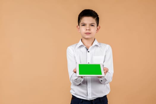 Little boy with tablet on light yellow studio background. he showing something on screen. space for text. moke up