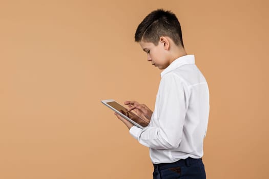 Little boy using tablet on light yellow studio background. space for text.