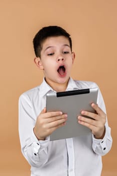 Little surprised boy using tablet on light yellow studio background.