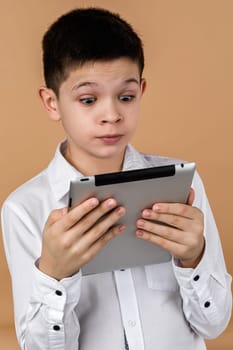 Little surprised boy using tablet on light yellow studio background.