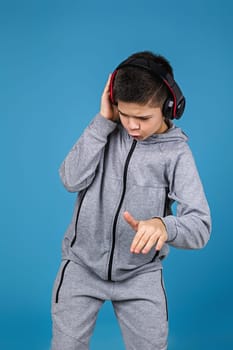 Happy child boy enjoys listens to music in headphones over blue background. boy dancing