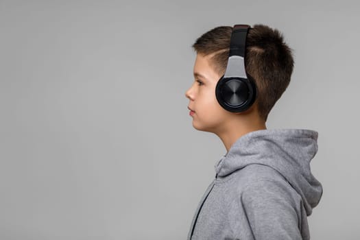 Happy child boy enjoys listens to music in headphones over gray background. copy space