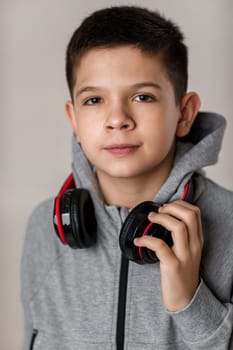 Happy child boy with headphones looking at camera over gray background.