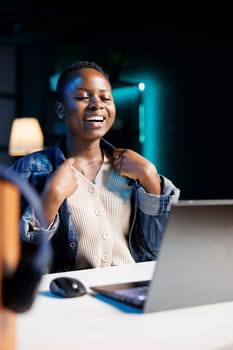 Black woman smiling wide and happily while using a digital personal computer in her apartment. Excited african american blogger seated in front of laptop, having a video conference call.