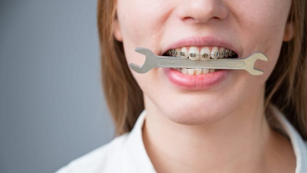 Close-up portrait of a woman with braces holding a wrench in her teeth