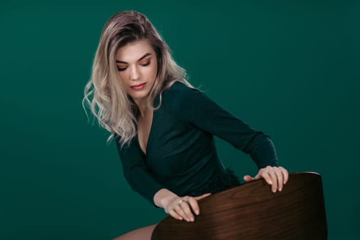 fashion portrait of beautiful blonde woman in green dress sitting on chair against green background. space for text